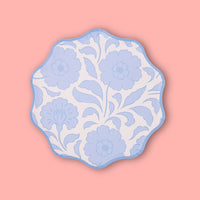 Single periwinkle-blue block-print floral scalloped paper plate on a pink background.