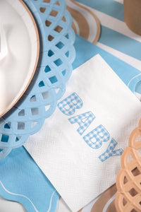 Blue gingham BABY napkin on a blue and tan striped table with a lattice charger and kraft cup