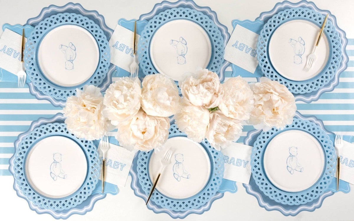 Overhead blue baby shower tablescape with blue gingham BABY napkins at six place settings and cream peonies
