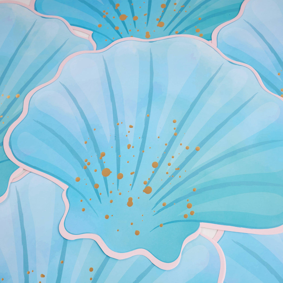 Overlapping blue seashell paper placemats showing the die-cut shell shape, ribbed detail, and gold foil accents.
