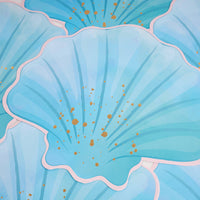 Overlapping blue seashell paper placemats showing the die-cut shell shape, ribbed detail, and gold foil accents.