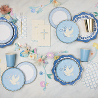 Blue trellis bow scalloped paper plates layered with navy dove plates and floral print plates on a baptism tablescape with cross napkins, gold paper cups, and pastel paper flower garland.
