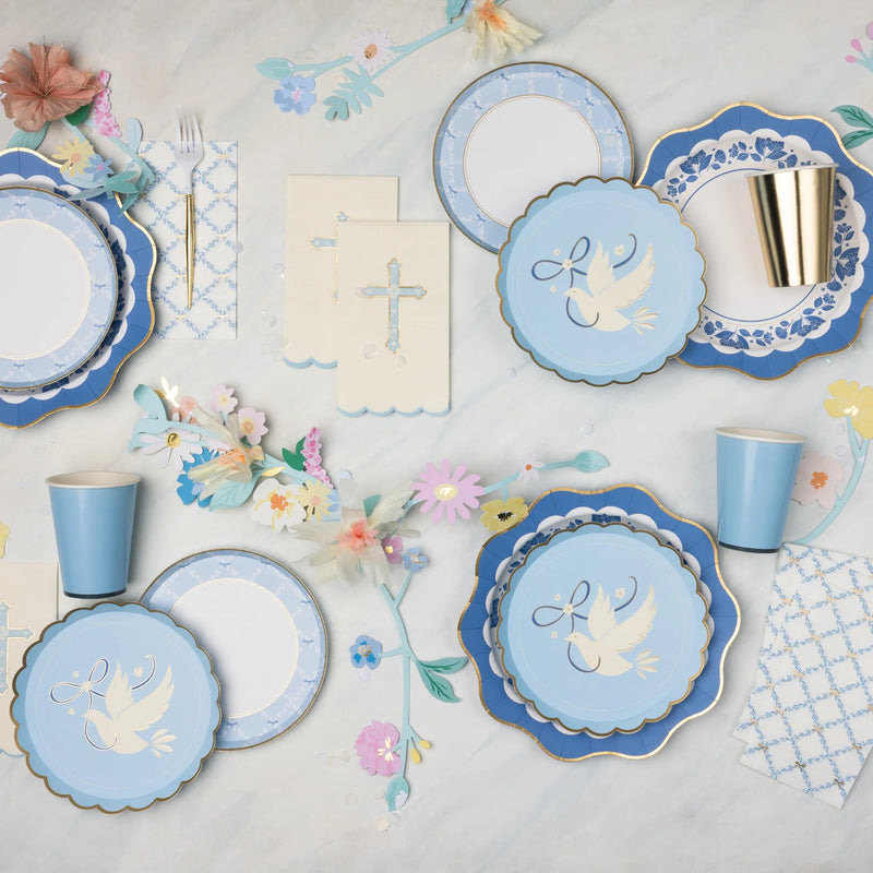 Blue trellis bow scalloped paper plates layered with navy dove plates and floral print plates on a baptism tablescape with cross napkins, gold paper cups, and pastel paper flower garland.