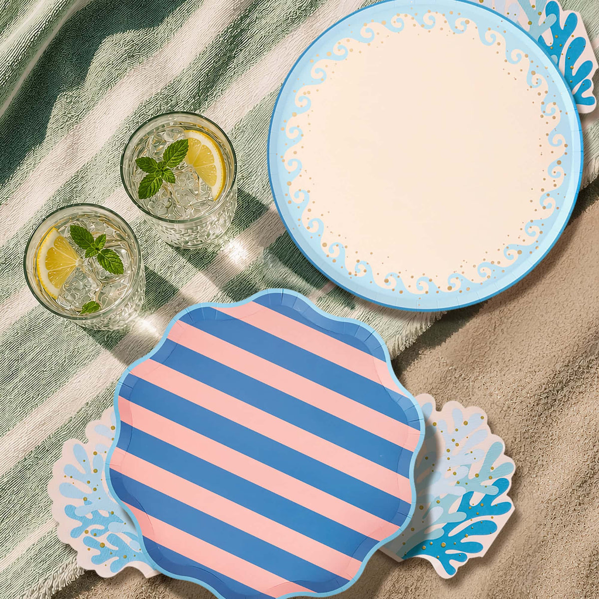 Blue wave dinner plate layered under a crab plate and coral napkin on a woven placemat with rose-gold cutlery.
