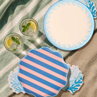Blue wave dinner plate layered under a crab plate and coral napkin on a woven placemat with rose-gold cutlery.
