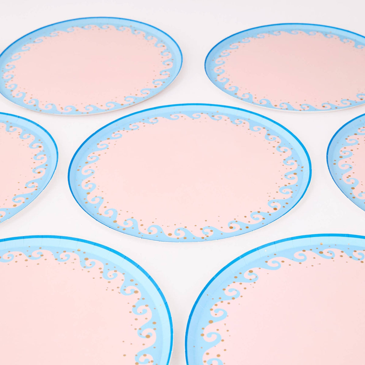 Group of blush-pink wave scalloped paper dinner plates with light-blue wave borders and gold foil dots.