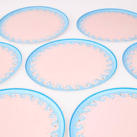 Group of blush-pink wave scalloped paper dinner plates with light-blue wave borders and gold foil dots.