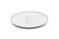 Edge of a cream teddy bear paper plate with a thin blue rim and the bear print in soft blue