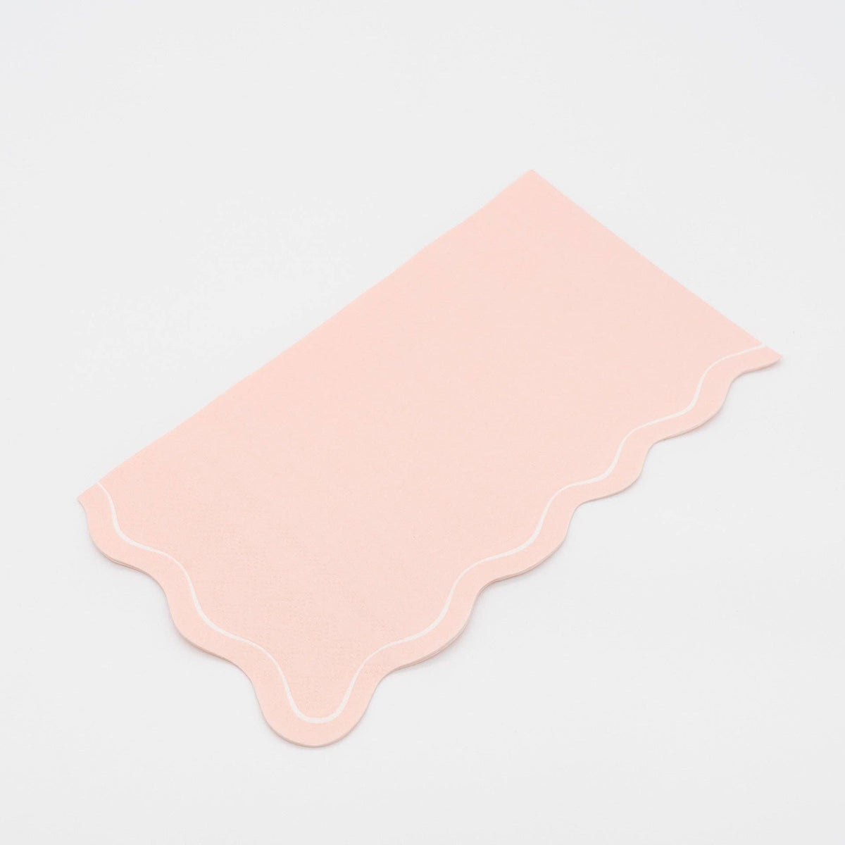 Folded blush pink guest towel on a plain surface showing the pink color and scalloped edge.