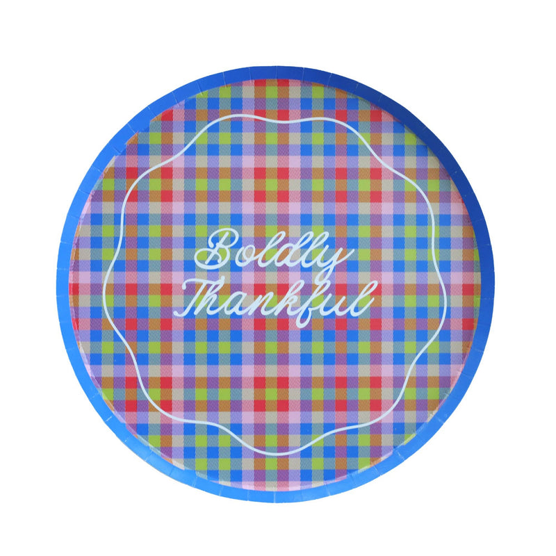 Top-down studio shot of a 10 inch round paper dinner plate featuring a colorful plaid pattern, a solid blue rim, and the phrase Boldly Thankful in white script.