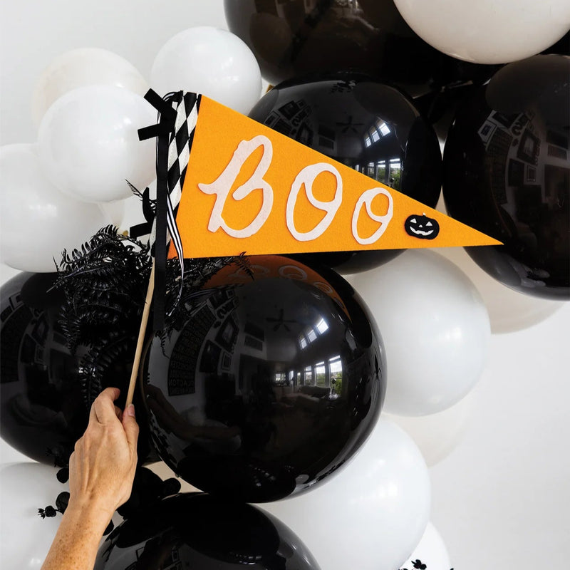 Hand holding orange Boo felt Halloween flag in front of black and white balloons.