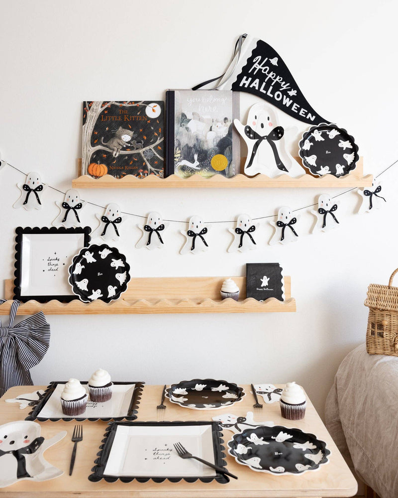 Halloween-themed room setting with black and white decorations on a wooden shelf featuring black ghost paper plate and other ghost decorations. 