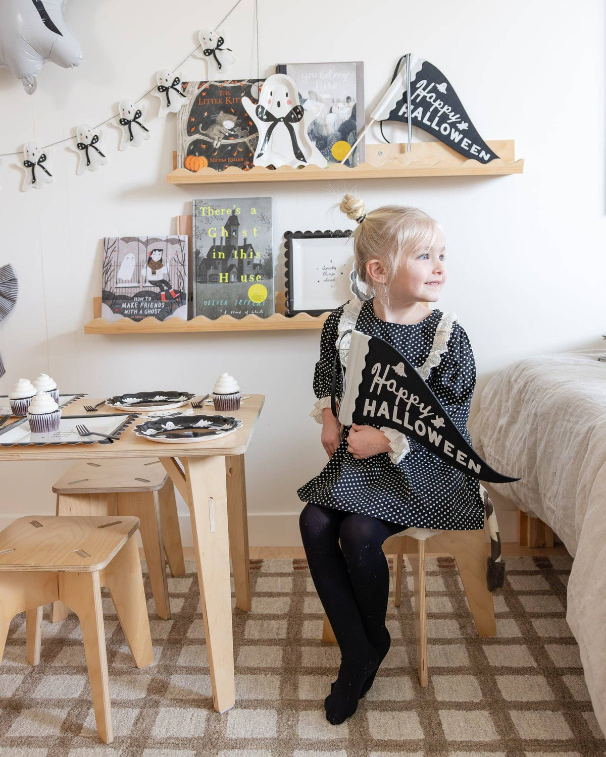 Child holding a 'Happy Halloween' banner in a room decorated for the holiday featuring Booquette ghost plates mixed with coordinating Halloween napkins on a cute Halloween tablescape.