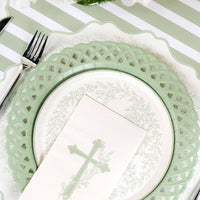 An angled close up of a botanical cross guest towel resting on an elegant floral and lattice paper plate.