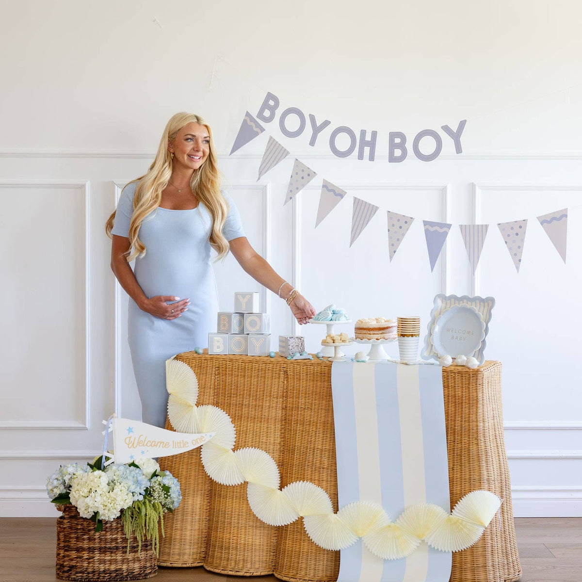 Pregnant mom posing next to baby blue “Boy Oh Boy” baby shower banner