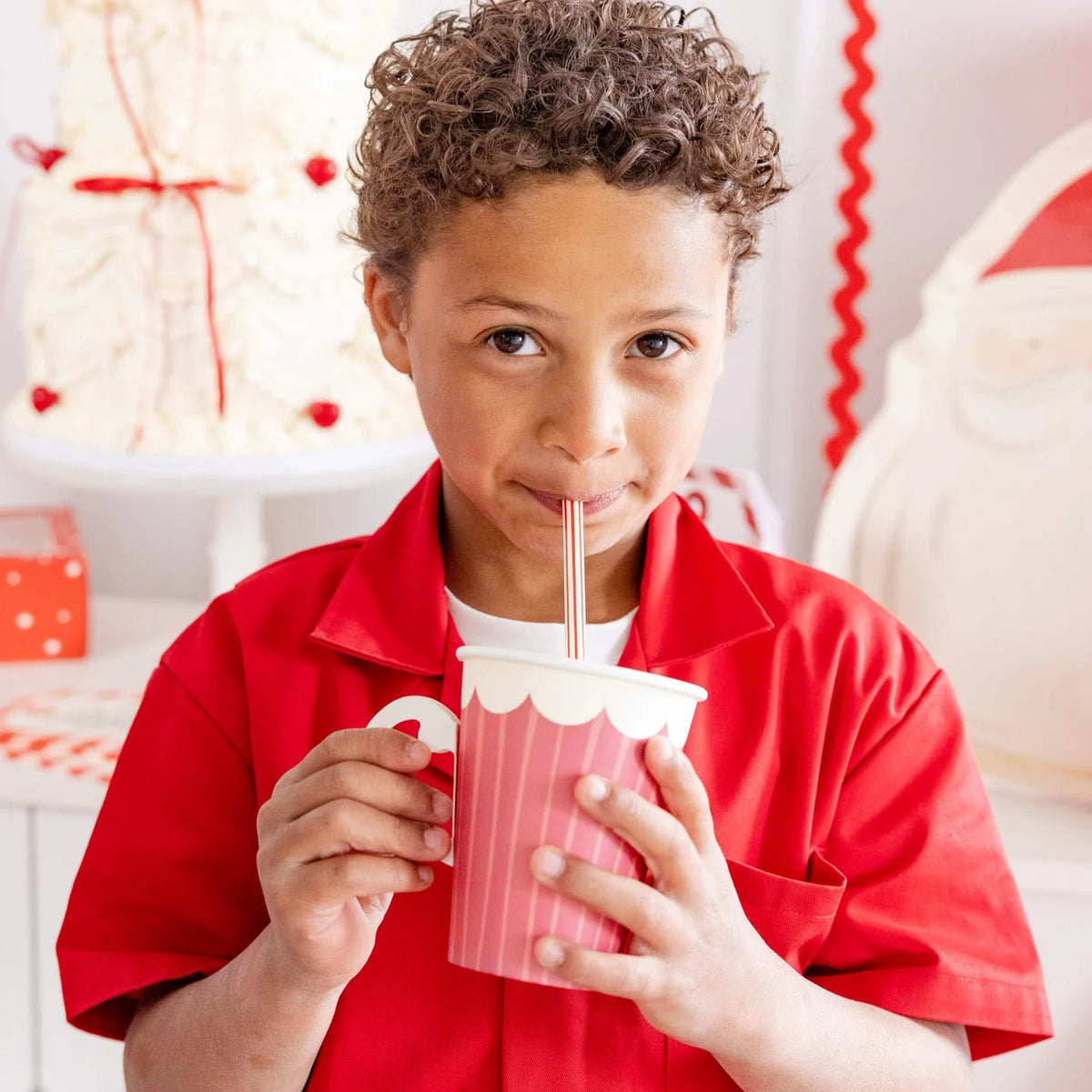 Portrait of a young boy with curly hair using a striped christmas straw at a holiday party.