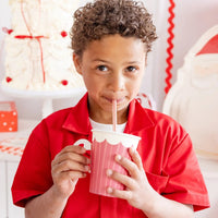 Portrait of a young boy with curly hair using a striped christmas straw at a holiday party.
