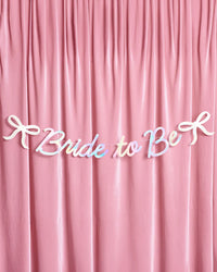 Full Bride to Be iridescent foil banner with bow accents hung on pink velvet backdrop