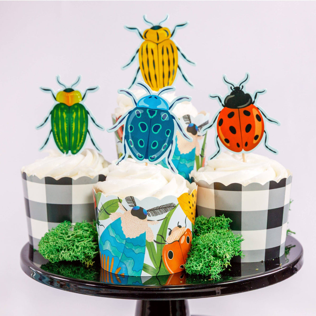 Bug cupcake kit styled on a black cake stand with beetle and ladybug toppers and gingham cups