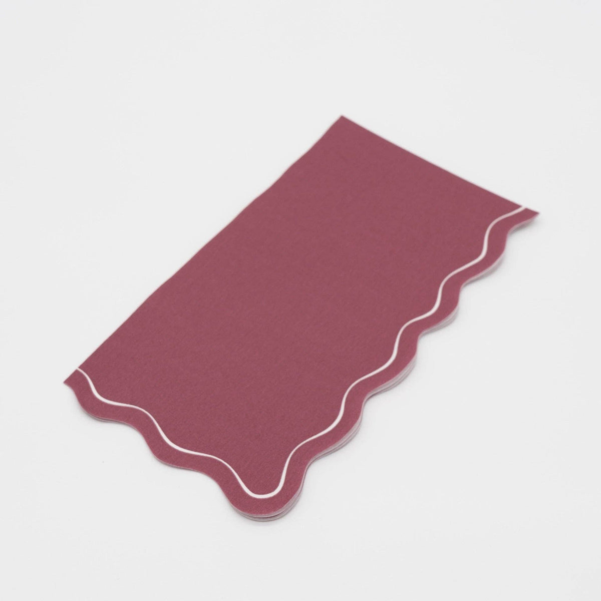 Folded burgundy guest towel on a plain surface showing the wine color and wavy scalloped edge.