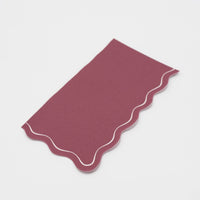 Folded burgundy guest towel on a plain surface showing the wine color and wavy scalloped edge.