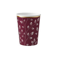 Burgundy paper party cup with an etched white leaf print and gold rim on a white background