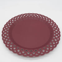 Angled close-up of a deep burgundy paper dinner plate showing the solid wine-colored center, raised rim, and intricate woven lattice cutout border.