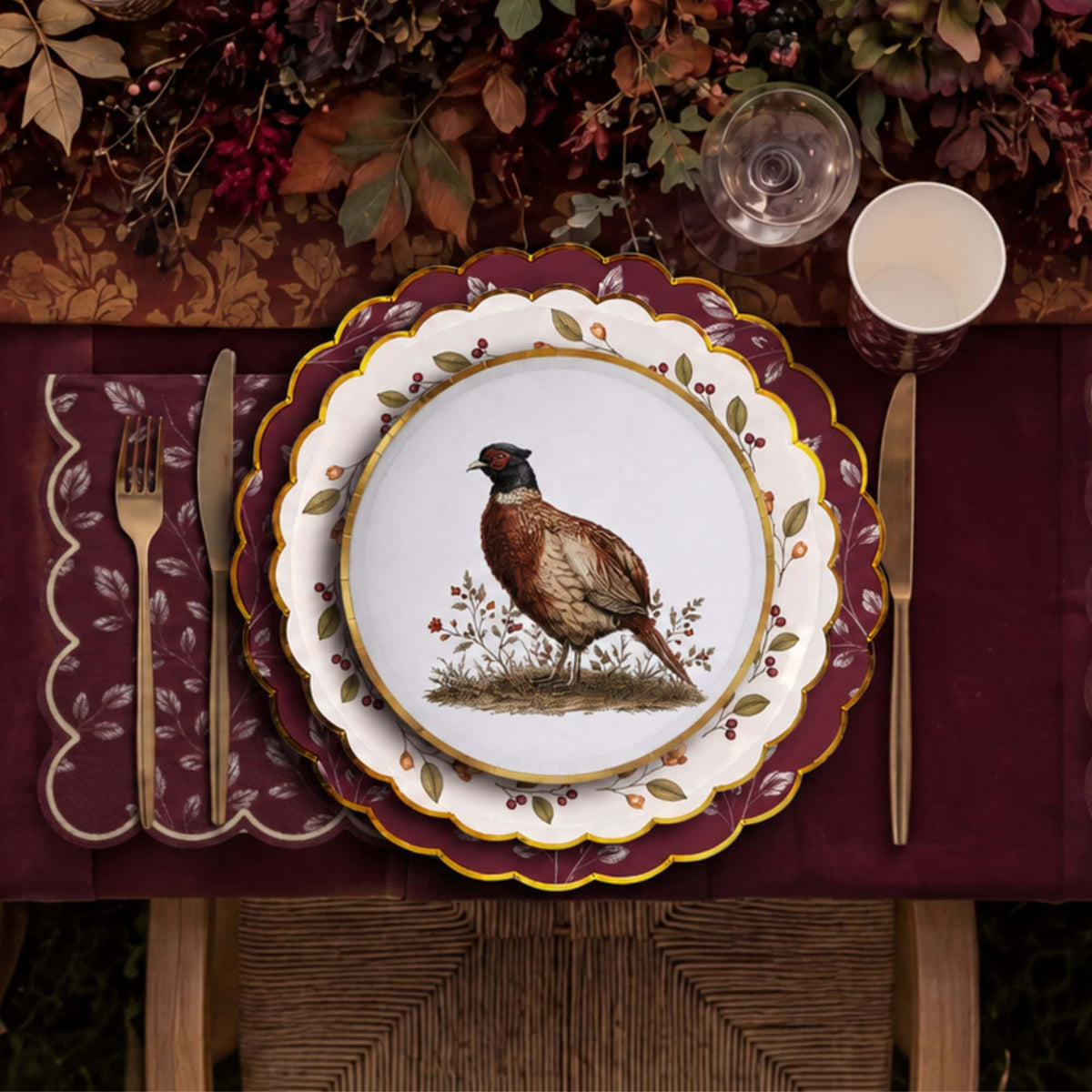 Overhead fall place setting with a burgundy leaf cup, gold flatware, and a dark floral centerpiece
