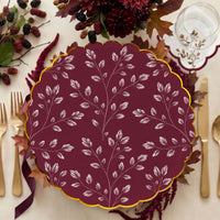 Burgundy leaf plate at a place setting with gold flatware, dark dahlias, blackberries, and a berry sprig napkin