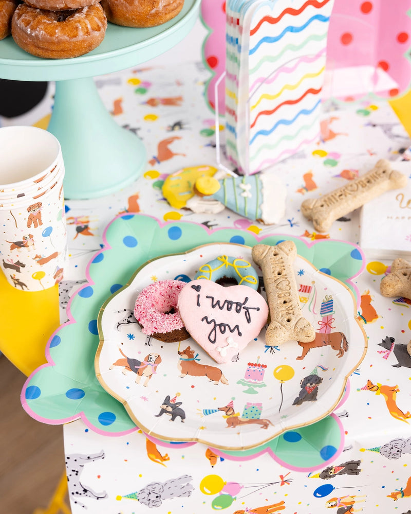 Party spread featuring mint polka dot plate, rainbow napkins, donuts, and dog-bone cookies on a patterned runner.