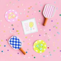 Pink backdrop with confetti, round ‘Let’s Pickle’ coasters, square pickleball napkin saying ‘Hit Me With Your Best Shot’, and paddle‑shaped plates.