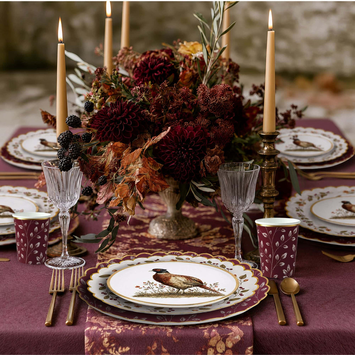 Candlelit fall table set with layered pheasant, berry wreath, and burgundy leaf plates and burgundy leaf cups