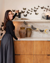 Host styling a Halloween party backdrop, hanging the pre-stitched celestial moth banner above a decorated marble counter with black wall moths.
