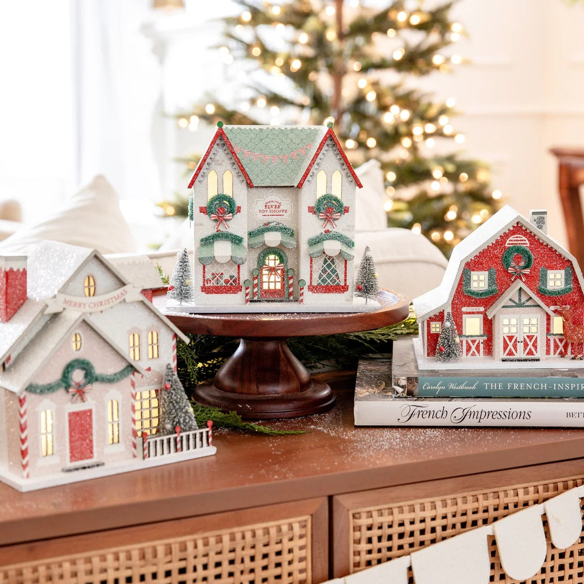 Central piece in the Christmas village display, showing the Elves' Toy Shoppe prominently on a wood cake stand near a holiday tree.