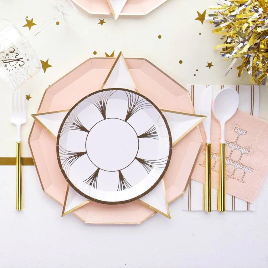 Roaring 1920s NYE tablescape with blush decagonal dinner plate, white star-shaped plate, gold foil champagne coupe paper plate, and blush champagne tower cocktail napkin styled with gold flatware and gold tinsel