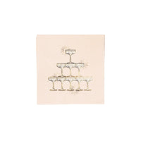 Single blush cocktail napkin printed with a gold foil champagne tower of stacked coupe glasses and sparkle accents on a white background