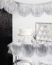 Champagne tower shaped plates styled on a party table with a cake and silver fringe backdrop