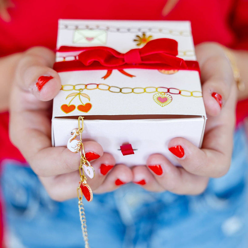 Hands holding a finished Charm Bracelet Kit gift box with Valentine charm designs and red ribbon.