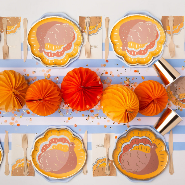 Long Thanksgiving tablescape with turkey-shaped plates, orange honeycomb pumpkins, and confetti.
