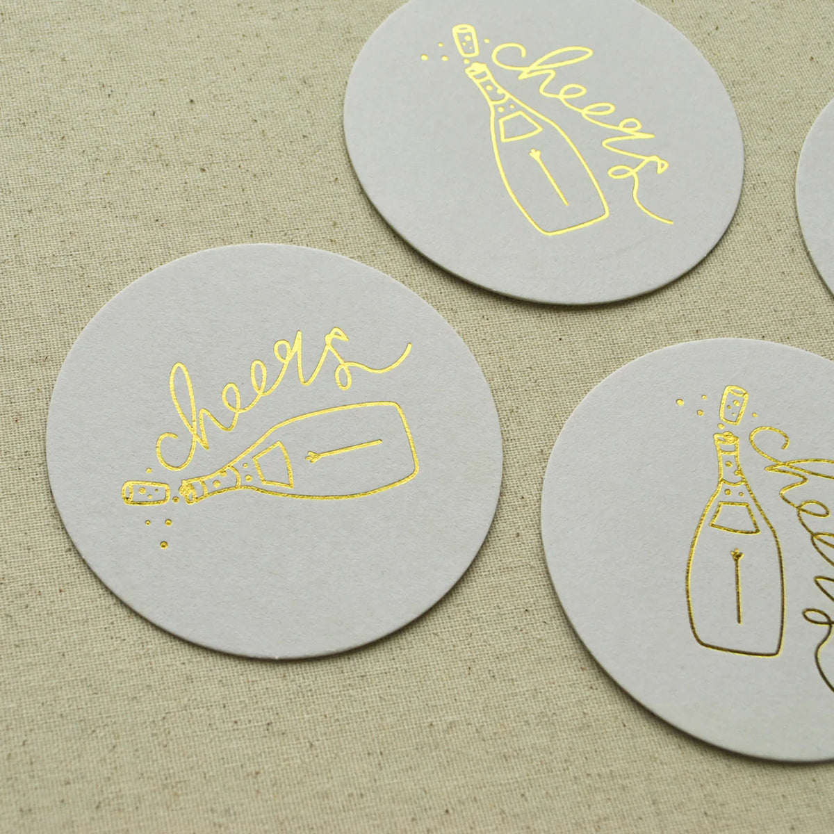 Round white Champagne Coaster with gold foil champagne bottle and cheers script.