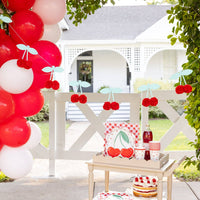 Cherry pom pom banner displayed near red and white balloons at a cherry themed party setup.
