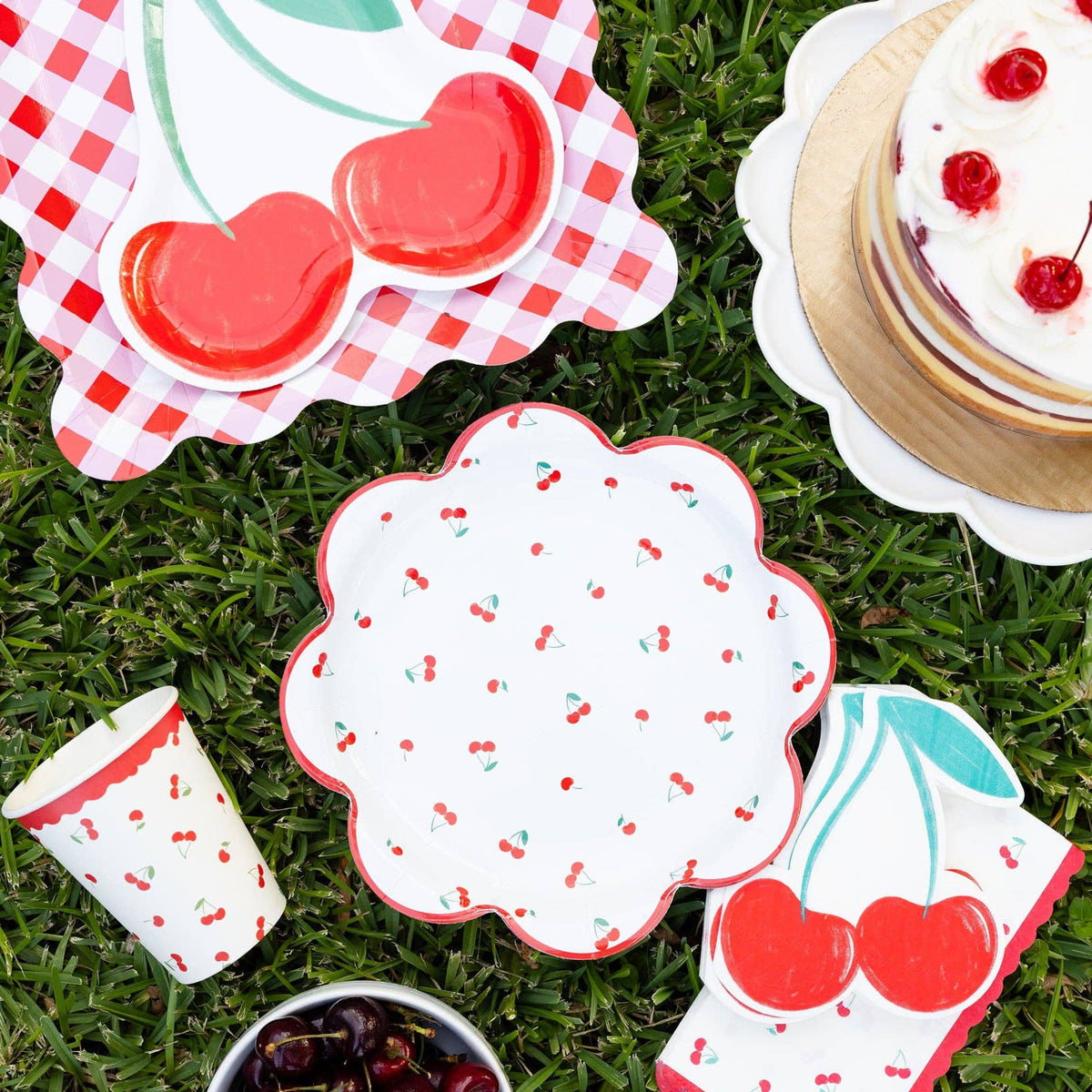 Cherry themed party picnic setup with cherry plates, cups, cake, and cherries on grass.

