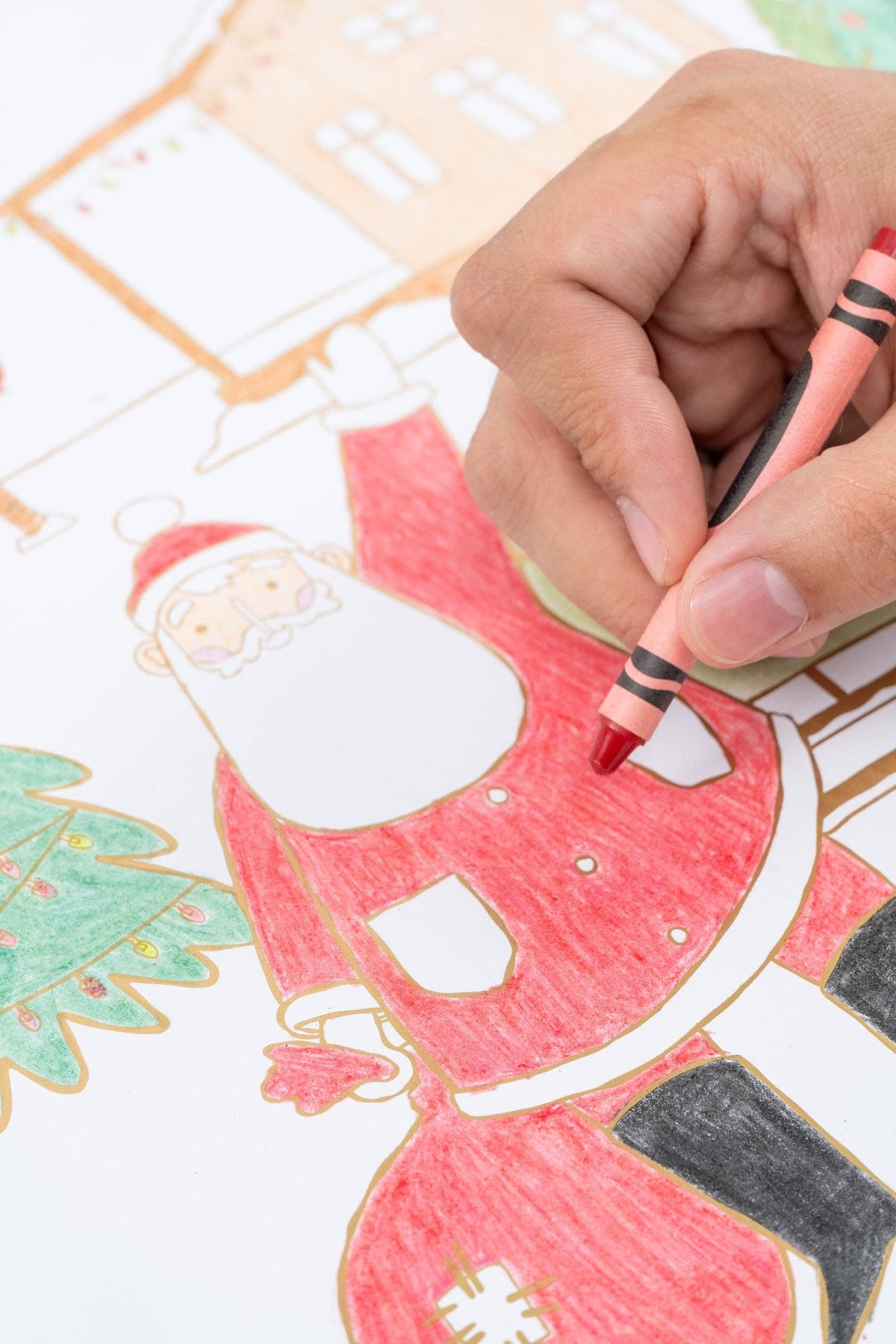 Close-up of a child's hand using a red crayon to color Santa's suit on the paper placemat.