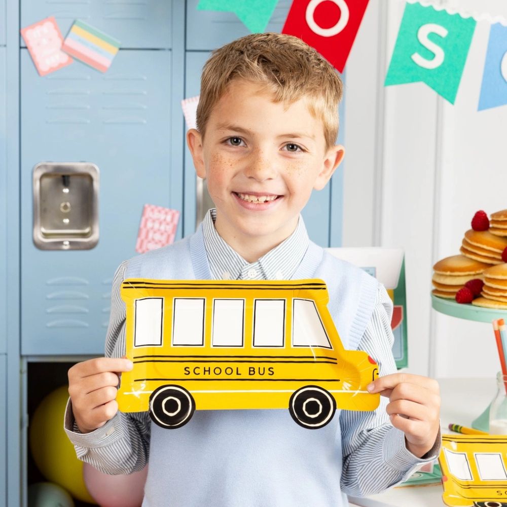 Child holding school bus shaped plate at party.