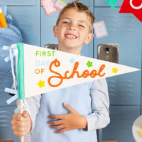 Child holding first day of school pennant smiling.