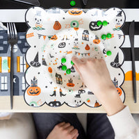 Overhead shot of child’s hand picking green candies from layered Tricks & Treats Halloween plates.
