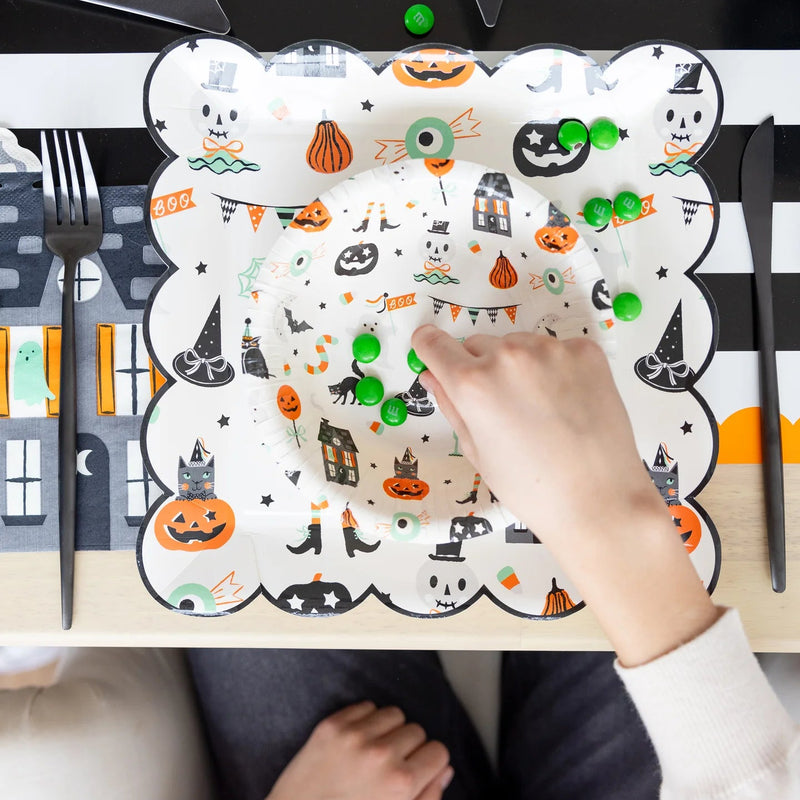 Overhead shot of child’s hand picking green candies from layered Tricks & Treats Halloween plates.