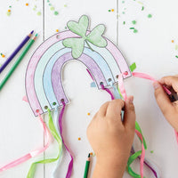Hands threading colorful ribbons through a rainbow craft project