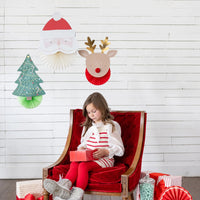 Lifestyle scene—girl in red chair under Santa, reindeer, and tree Christmas wall decor