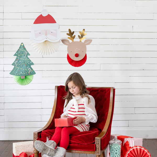 Lifestyle scene—girl in red chair under Santa, reindeer, and tree Christmas wall decor